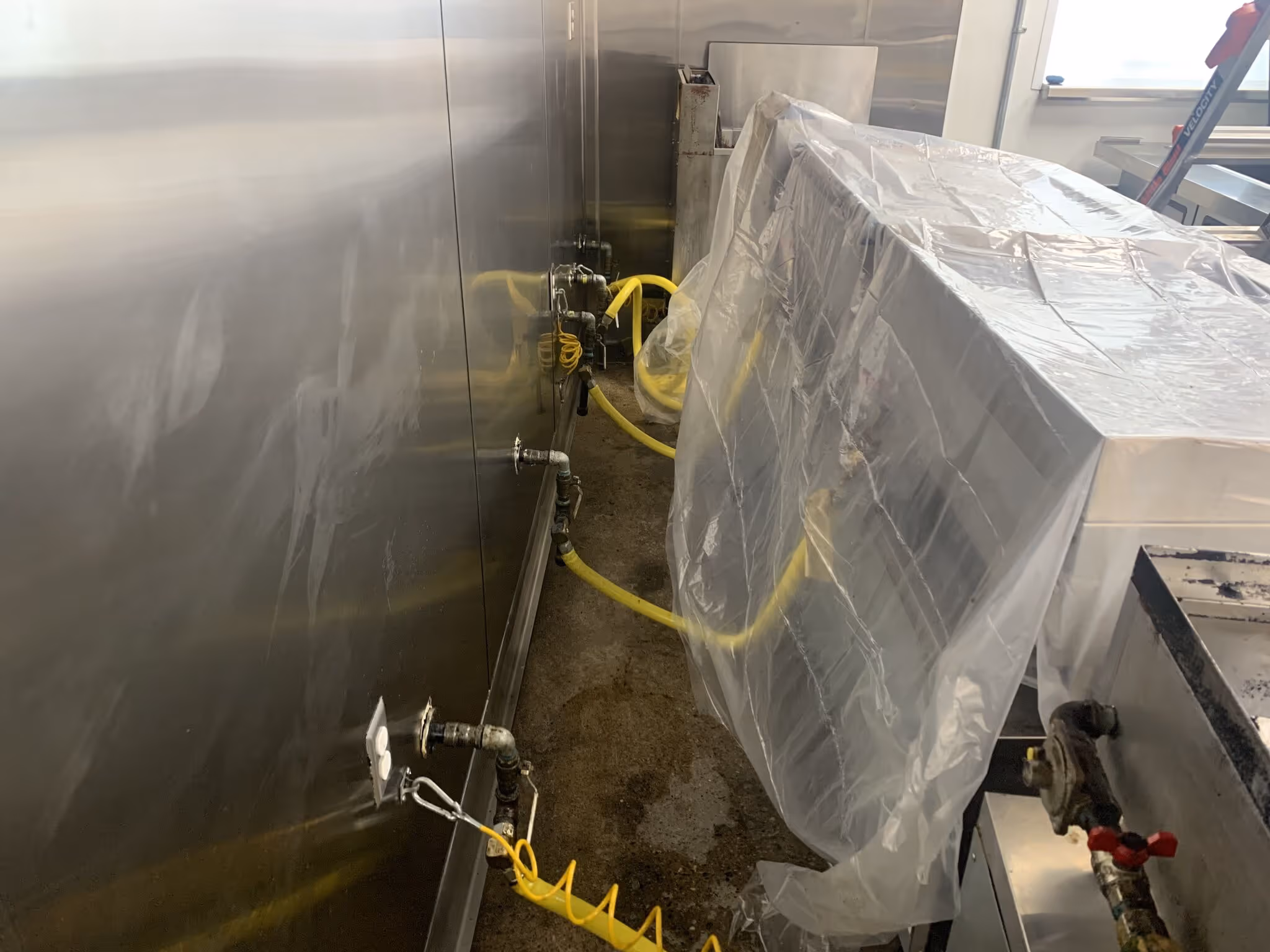 Industrial stainless steel equipment connected with yellow hoses in a utility room.