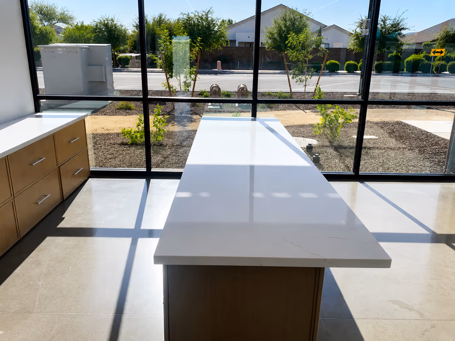 Empty modern kitchen with a white island countertop and wooden cabinets under large windows.