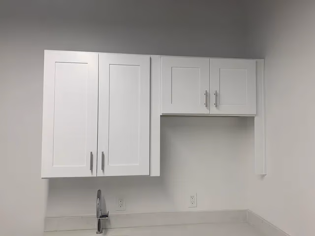 White kitchen wall cabinets mounted above a white countertop with a silver faucet and electrical outlets.