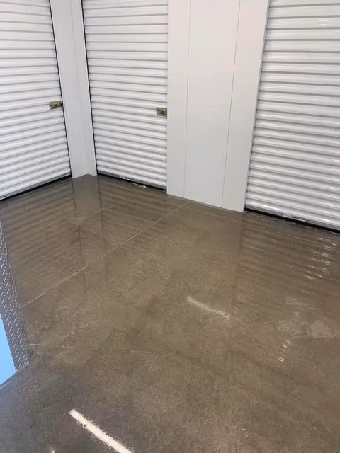 Empty storage unit area with closed white metal roll-up doors and polished concrete floor.