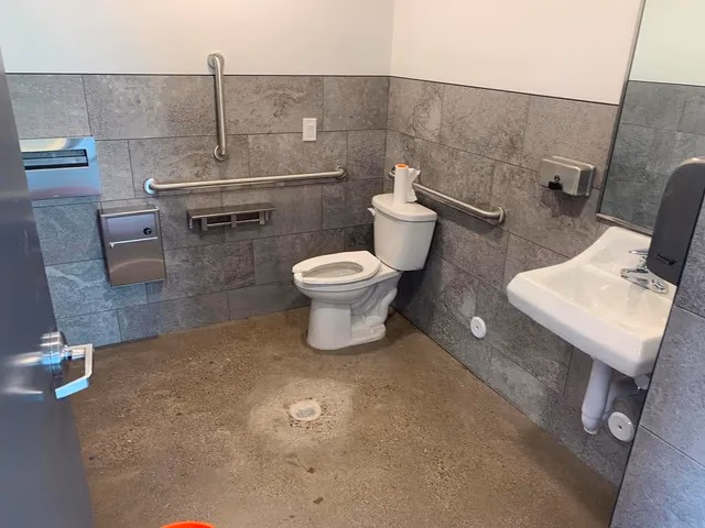 Clean, accessible public restroom with a toilet, sink, handrails, soap dispenser, and paper towel holder.