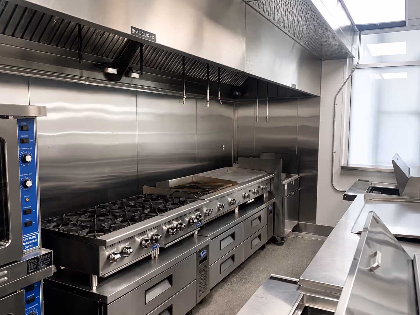 Clean commercial kitchen with large stainless steel stove, oven, fryer, and ventilation hood.